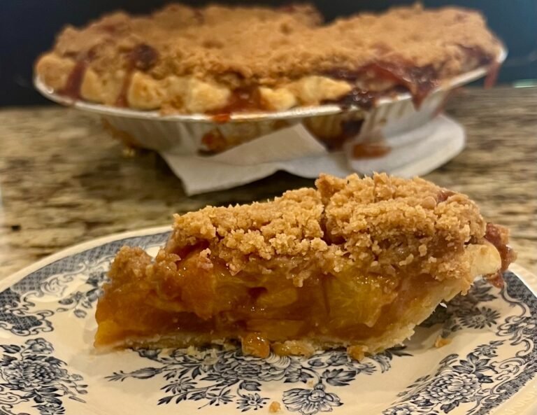 Slice of homemade 6-inch peach bourbon crumble pie with golden brown topping and layered peach filling.